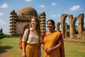 A bright travel photograph of international tourists and a local guide exploring the historic Islamic and Chalukyan architectural heritage sites in Bijapur, Karnataka.