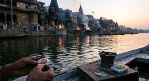 Varanasi ghats at dawn with cremation fires visible in middle distance and river reflecting first light photographed from the water