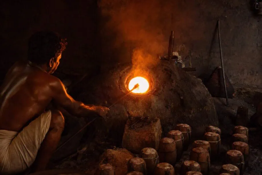Ancient crucible steel furnace glowing orange in South Indian forge with sealed clay crucibles in foreground showing Wootz steel production process that became Damascus steel