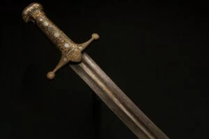 Extreme close-up of Damascus steel blade surface showing characteristic wavy banding pattern of Wootz steel from South India catching light at low angle against dark background